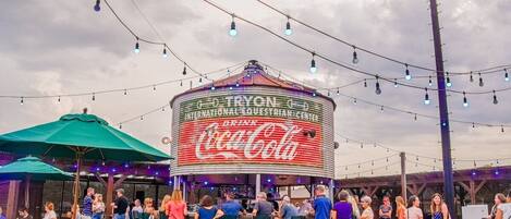 An outdoor seating area with tables and umbrellas, a Coca-Cola branded structure, and string lights.