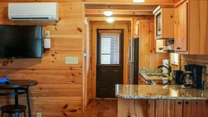 Interior de una cabaña de madera con cocina, una mesa de comedor y una televisión.
