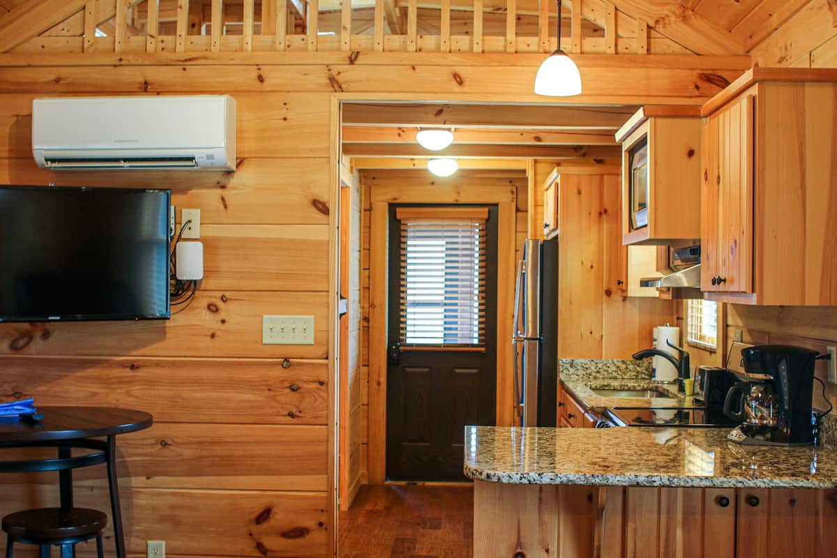 A wooden cabin interior with a kitchen area, a dining table, and a television.