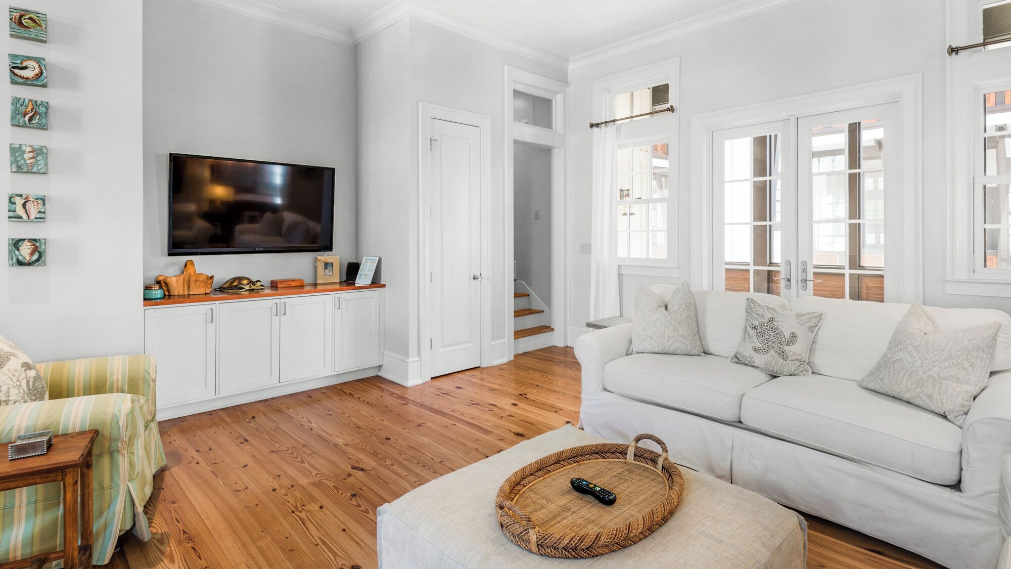 A spacious living room with a flat-screen TV, white cabinets, a white sofa, and a wooden floor.