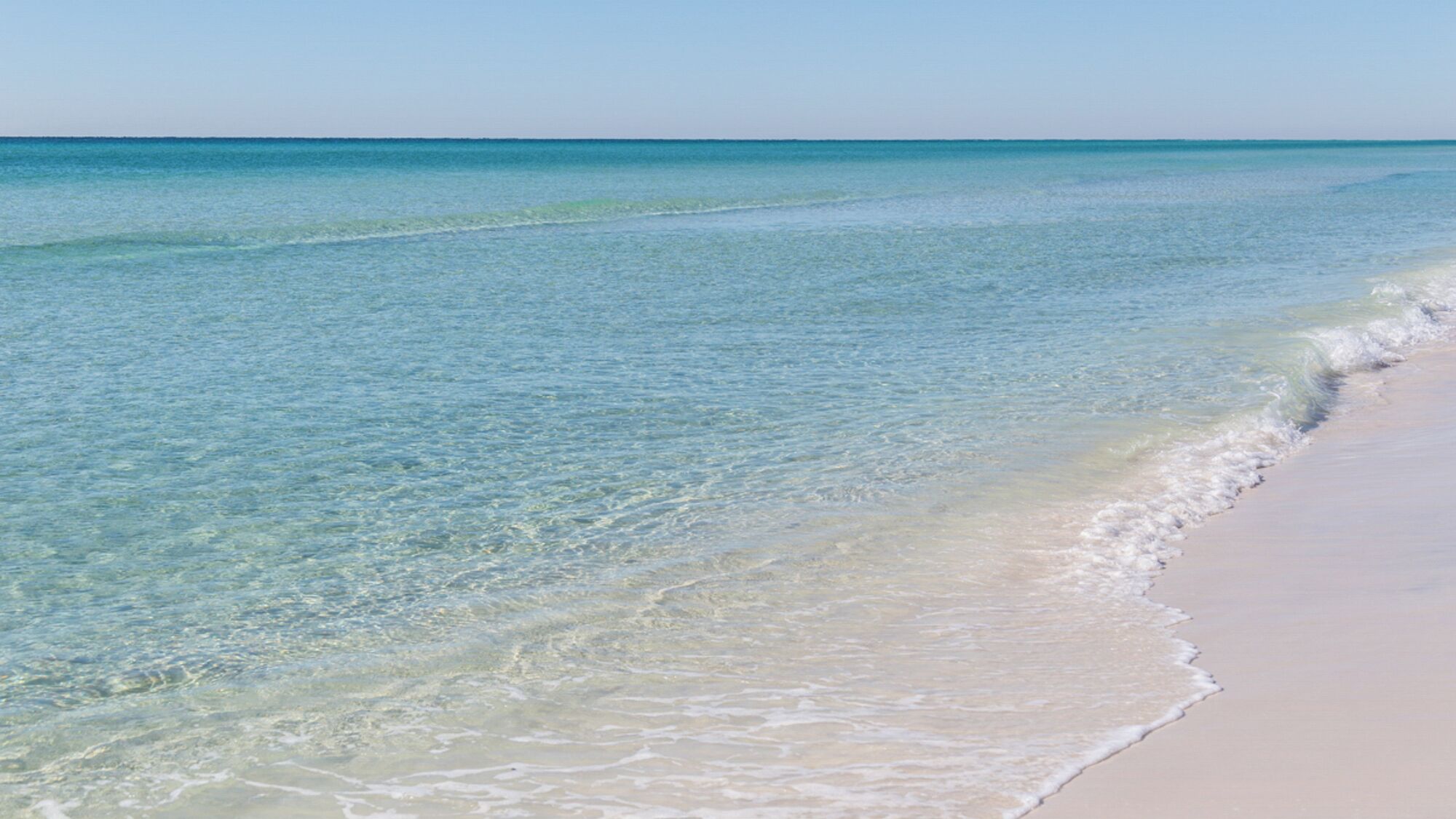 A beach with clear shallow waters and a sandy shore.