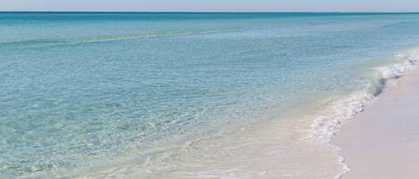 A beach with clear shallow waters and a sandy shore.
