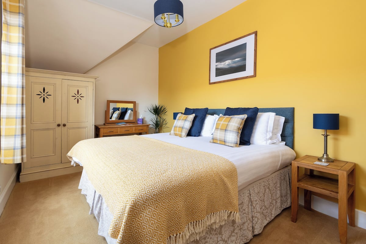 Quarto com cama grande, mesa de cabeceira, luminária, espelho e guarda-roupa.