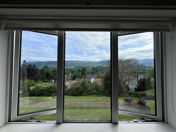 A room with a large window offering a view of a green landscape with trees and a distant hill.