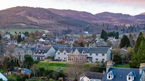 A residential area with stone houses, a grassy lawn, and a backdrop of hills. - Beinn Bhracaigh (Pitlochry)