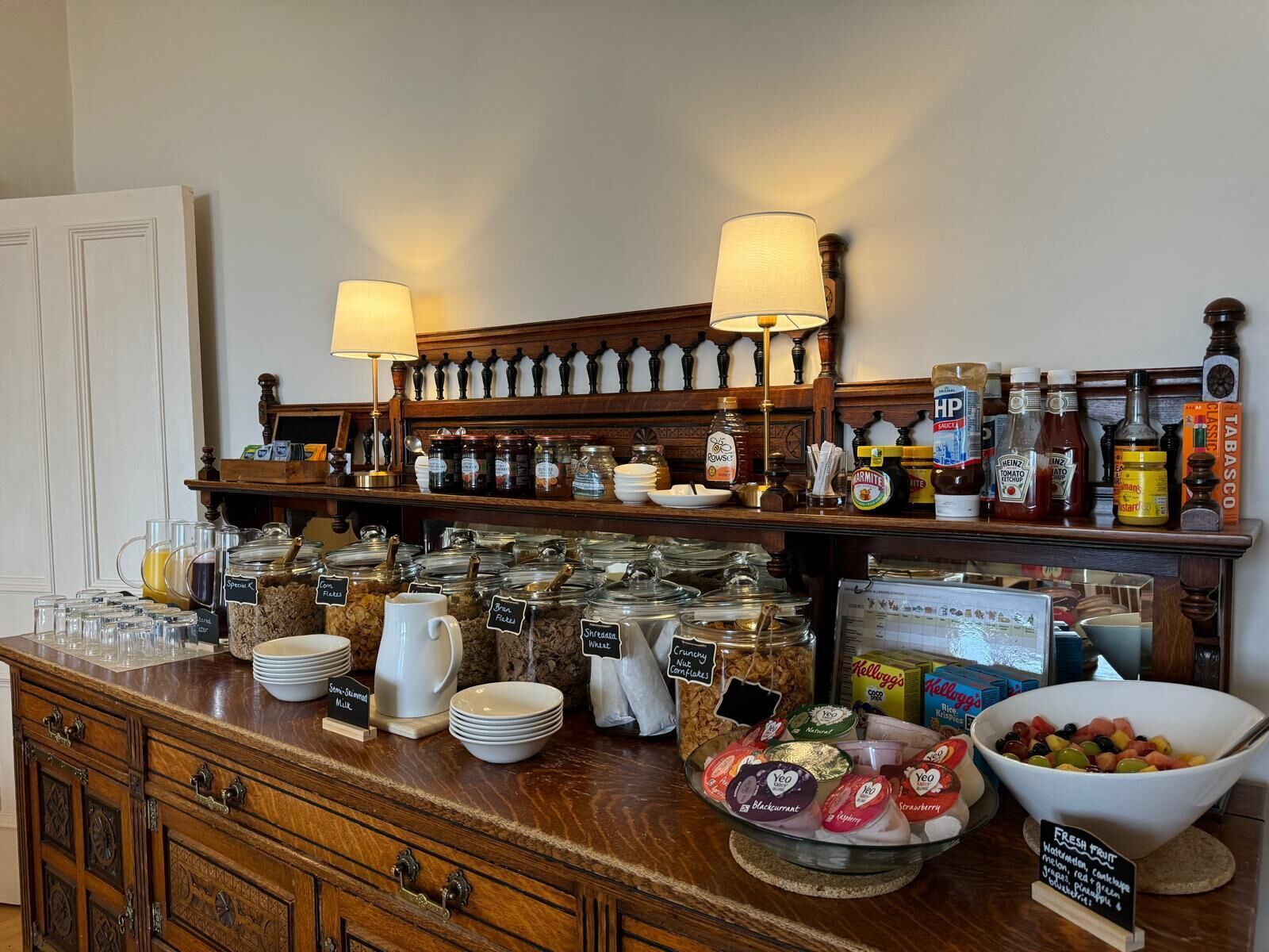 A breakfast buffet with various food items, condiments, and a fruit bowl.