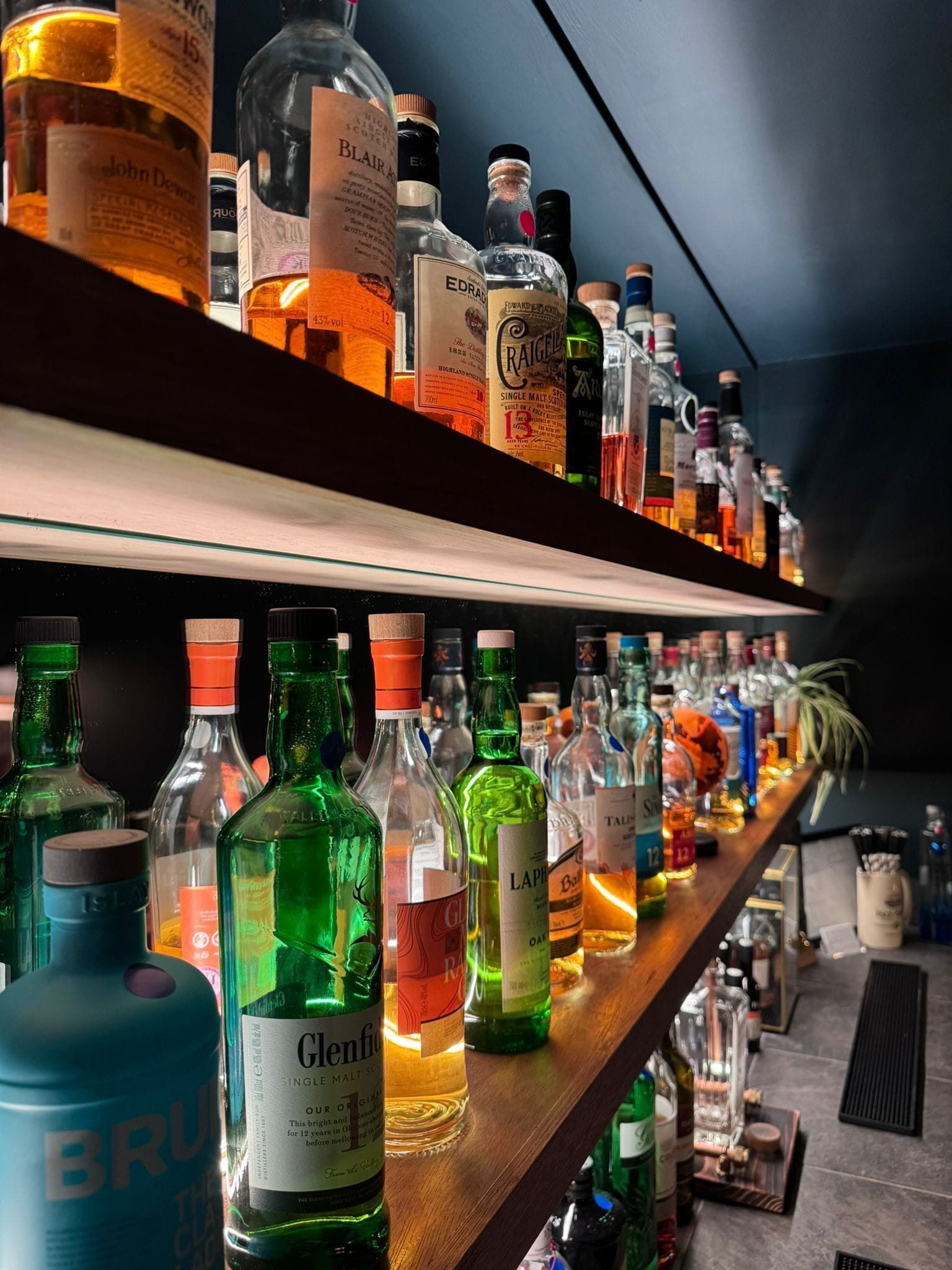 Bar com estantes cheias de garrafas de bebidas alcoólicas diversas.