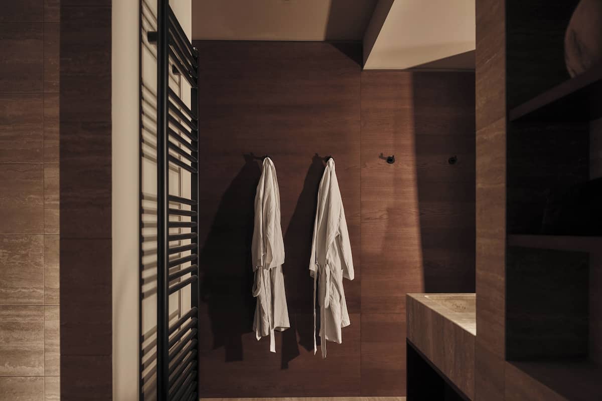A modern bathroom with wooden walls, a large mirror, and two towels hanging on a rack.