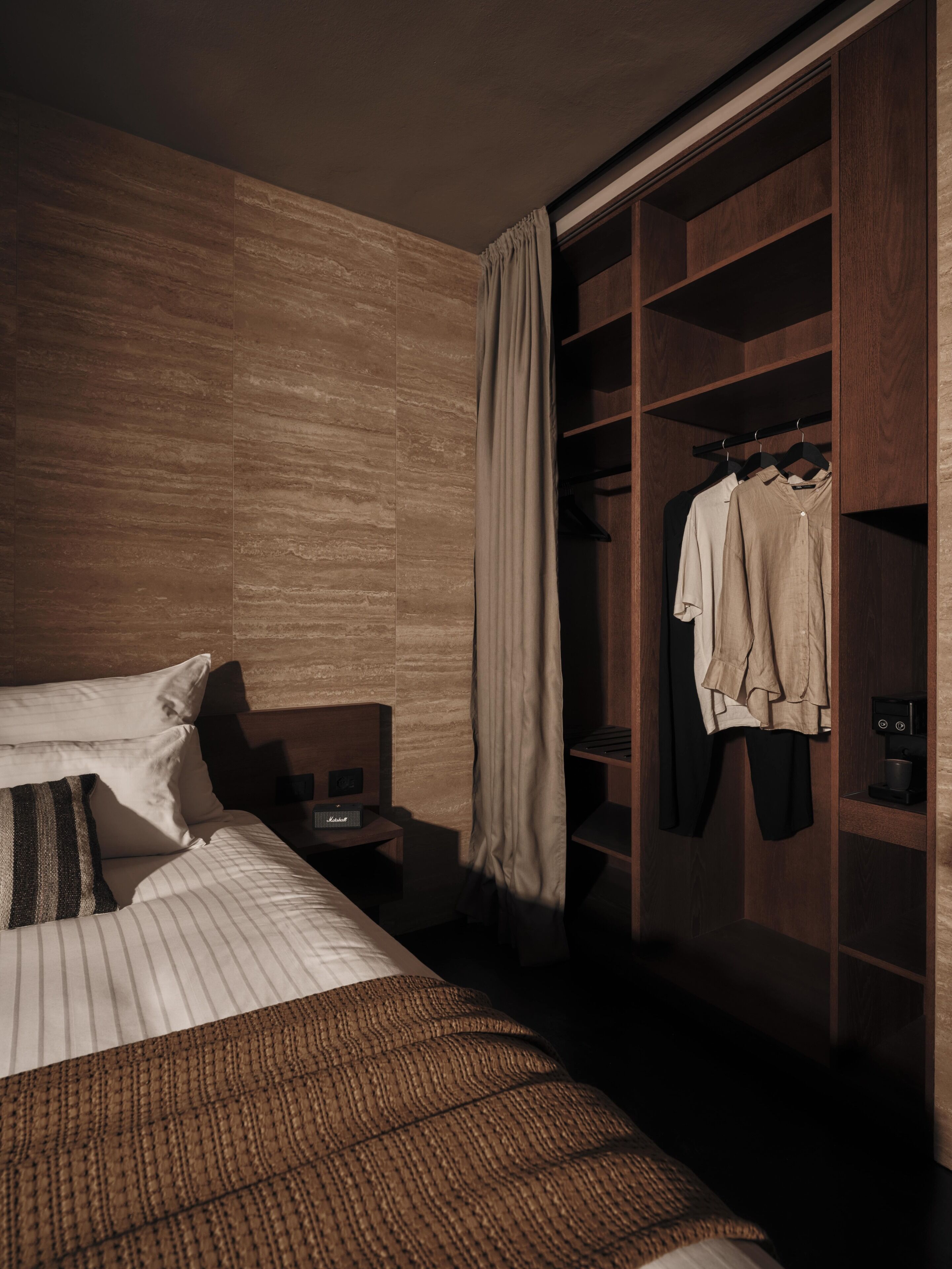Una habitación de hotel con una cama grande, un armario y una mesita de noche con lámpara.
