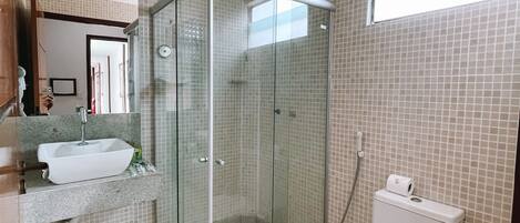 A bathroom with a glass-enclosed shower, a toilet, and a sink with a mirror above it.