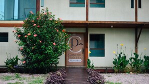 Der Hauseingang von Casa do Pedrinho auf Noronha, mit einem hölzernen Pfad, der zum Eingang führt, umgeben von üppiger Vegetation und blühenden Pflanzen.