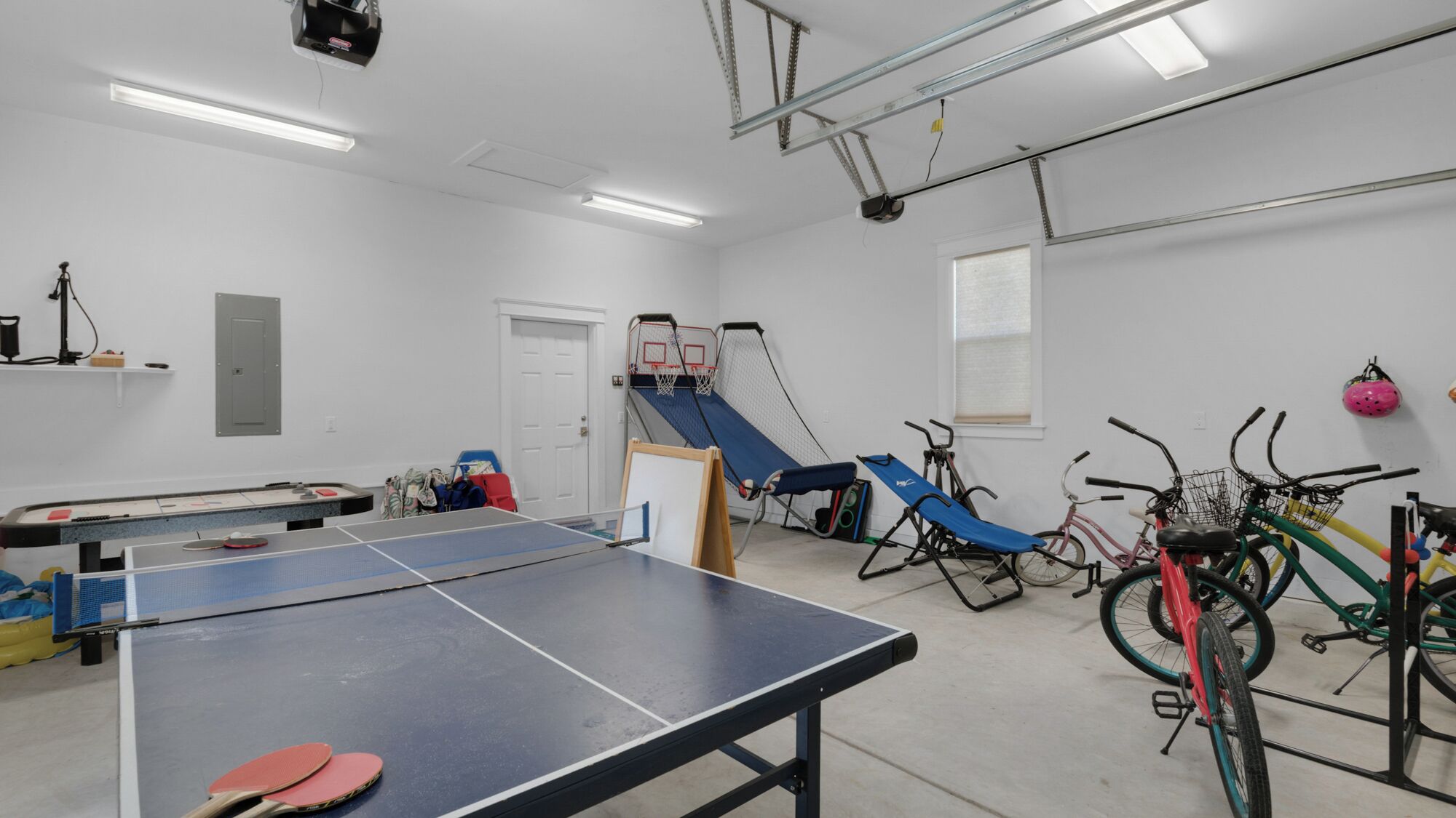 Una habitación con mesa de ping pong, equipo de ejercicio y bicicletas.