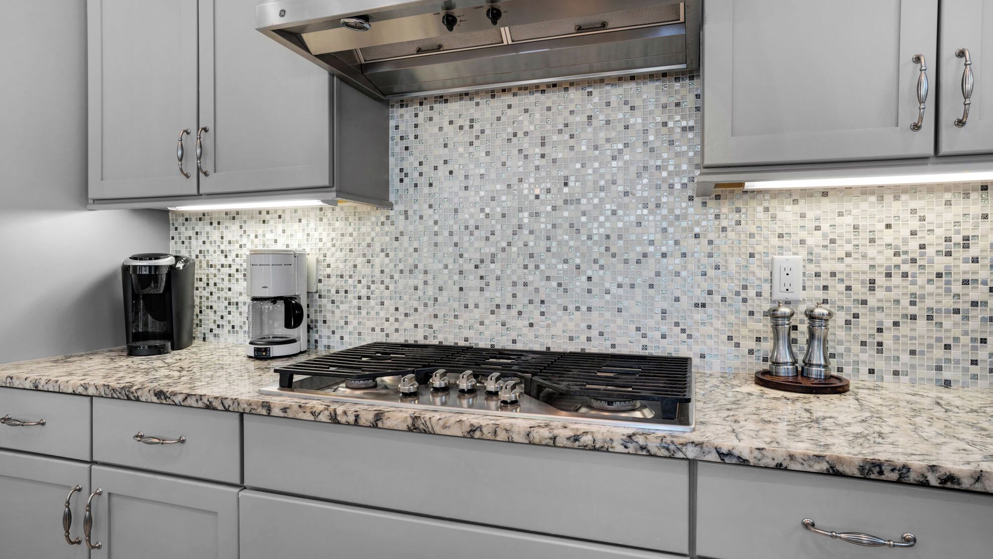 A modern kitchen with a gas stove, coffee maker, and a tiled backsplash.