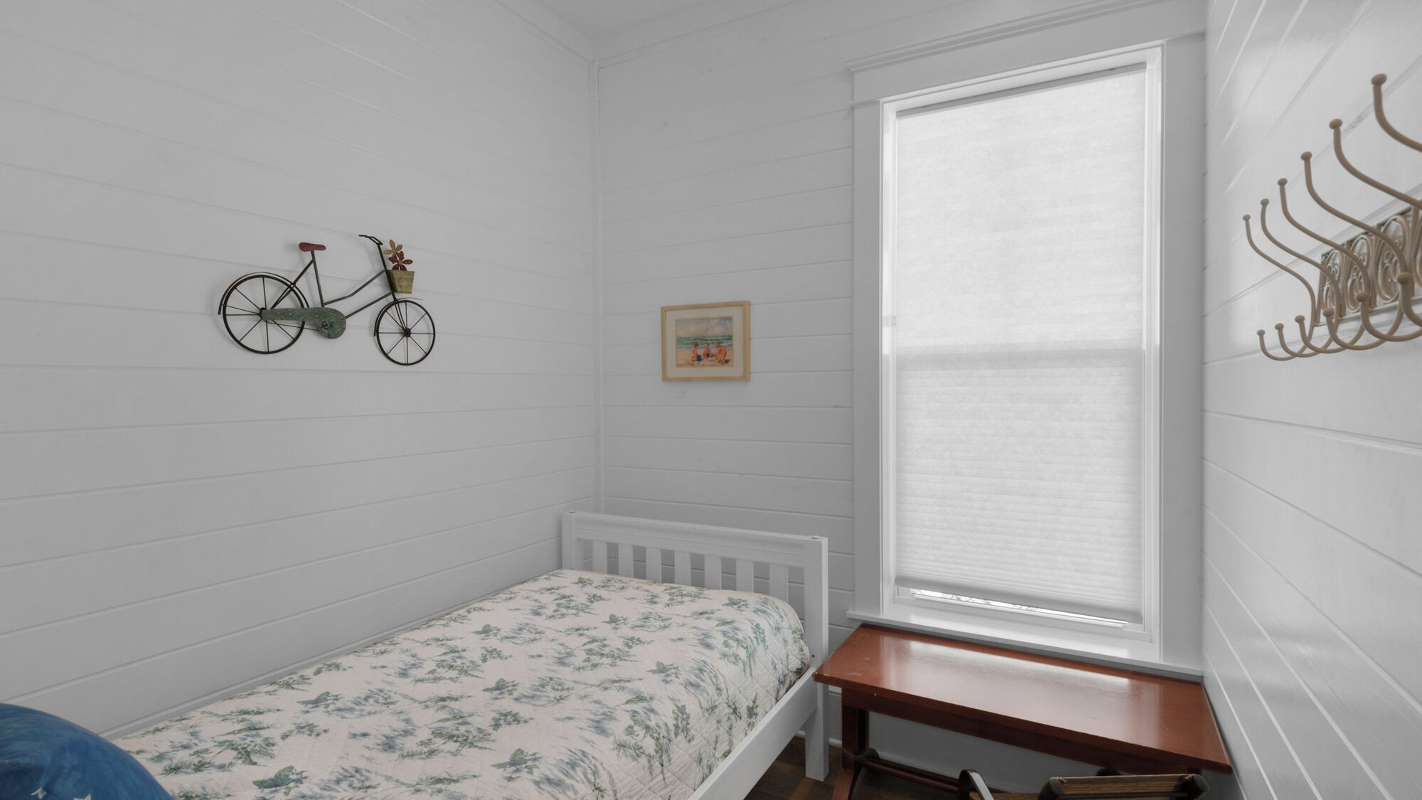 A small, single-bed room with a window, a bicycle decoration, and a picture on the wall.