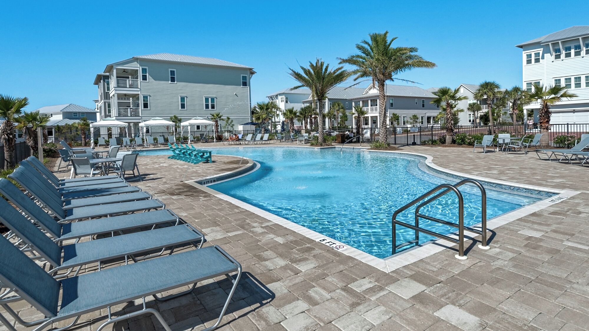 A swimming pool with lounge chairs, palm trees, and a building in the background.