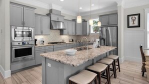 A modern kitchen with grey cabinets, stainless steel appliances, a granite island, and pendant lighting. - Modern Prominence Home ~ Game Room, 4 Bikes, Sleeps 13, Pet Friendly! (Santa Rosa Beach)
