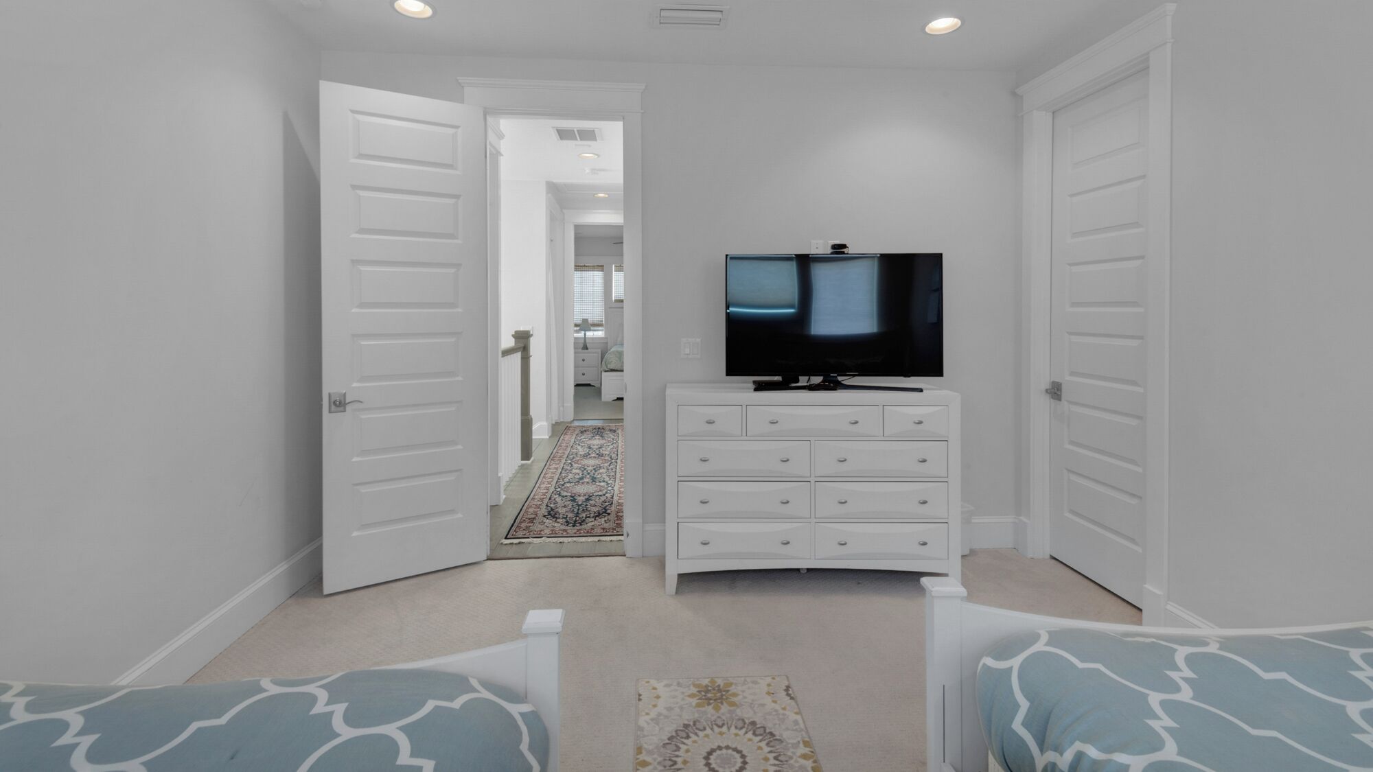 A bedroom with a television on a dresser, a door leading to another room, and a patterned rug on the floor.