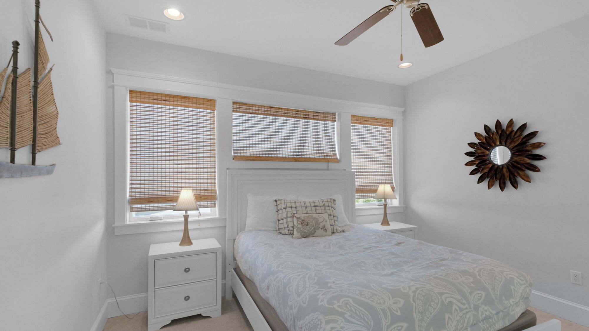 A bedroom with a bed, two bedside tables with lamps, a ceiling fan, and a decorative wall piece.