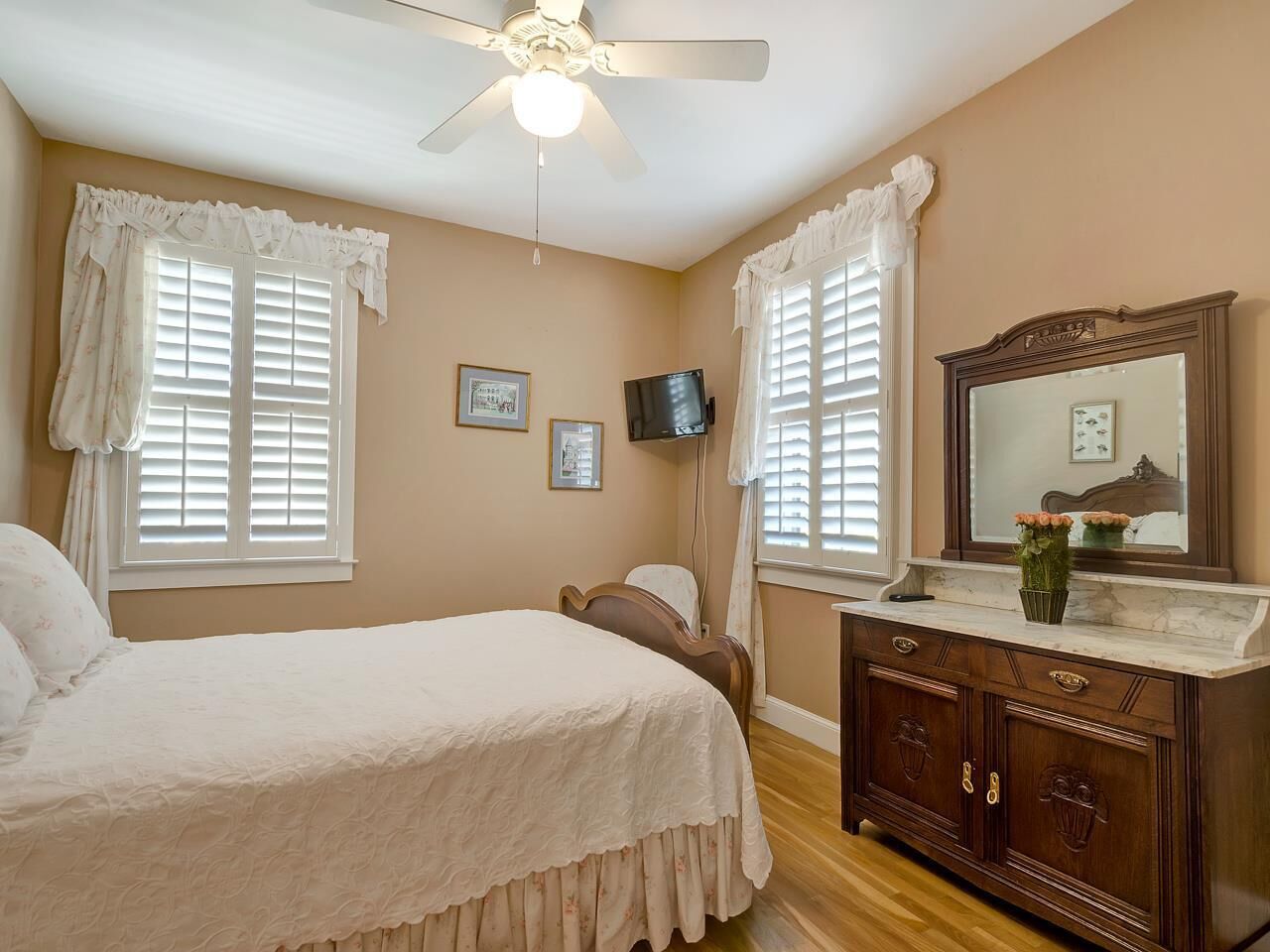 A bedroom with a bed, a dresser, a television, and two windows with curtains.