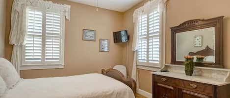 A bedroom with a bed, a dresser, a television, and two windows with curtains.