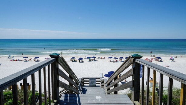 A wooden staircase leading to a beach with umbrellas and beach chairs.