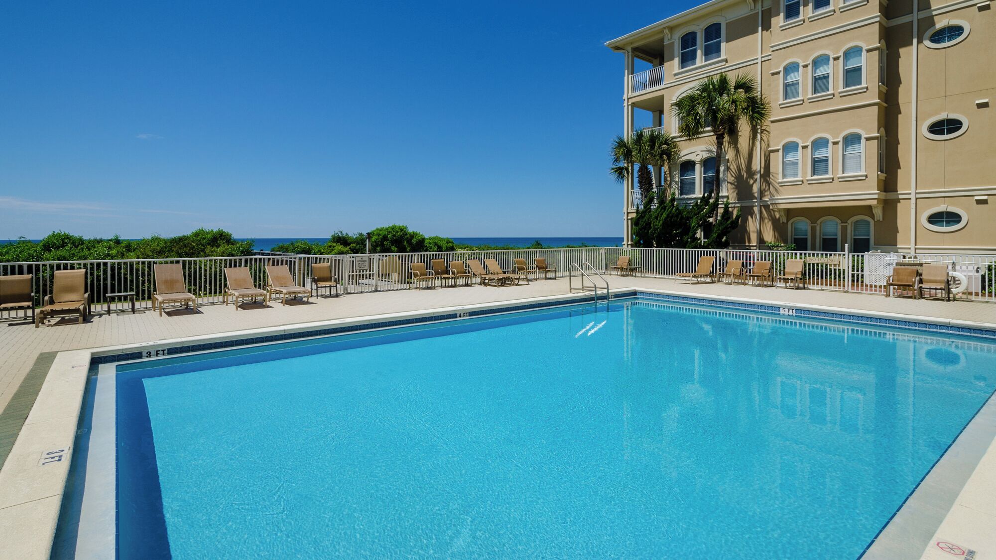 A rectangular swimming pool with a clear blue water surface, surrounded by a white poolside area with lounge chairs.