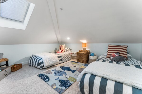 Una habitación infantil con dos camas, una ventana y una mesita de noche con lámpara.
