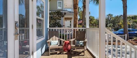 A covered porch with wooden chairs and a red basket.