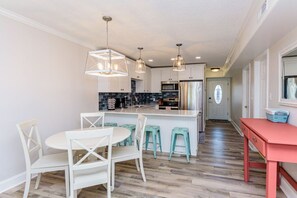Une cuisine moderne avec des meubles blancs, un îlot central doté de tabourets, un éclairage suspendu et un banc rouge.