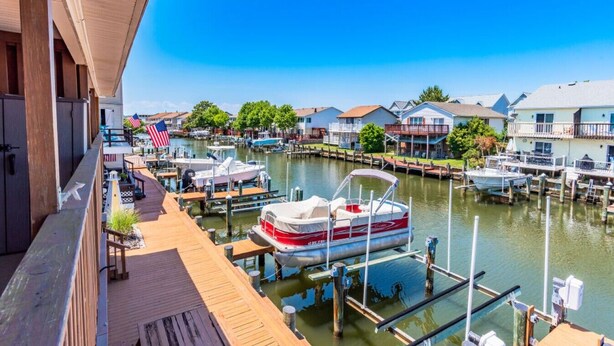 Un port de plaisance avec des bateaux amarrés, des maisons au bord de l’eau et une terrasse en bois.