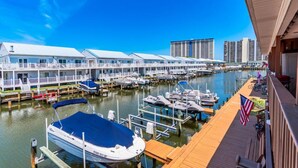 Un port de plaisance avec des bateaux amarrés, un bâtiment au bord de l’eau doté de balcons et un ciel bleu azur.