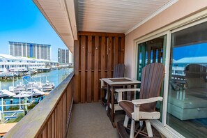 Ein Balkon mit Holzgeländern, einem Tisch, zwei Stühlen und Blick auf eine Marina mit Booten und Gebäuden im Hintergrund.