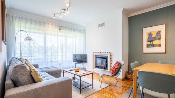 A modern living room with a sofa, a coffee table, a fireplace, a TV, and a dining area. - Infante Cozy 1BR w/ Parking by LovelyStay (Vila Nova de Gaia)