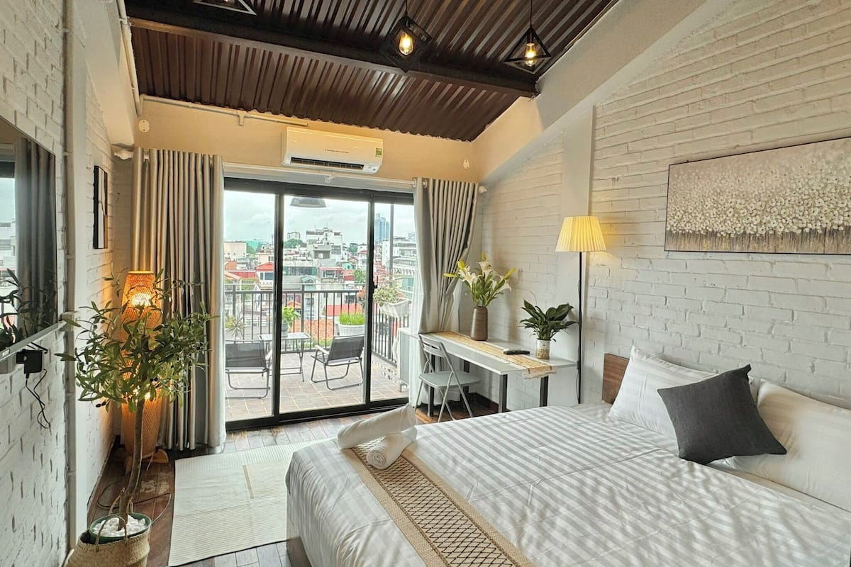 A hotel room with a bed, desk, and balcony with city views.