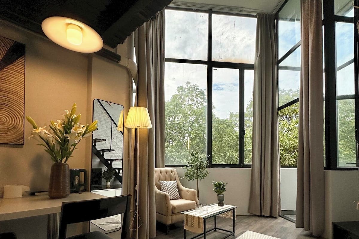 A modern living room with a dining area, large windows, and a view of greenery outside.