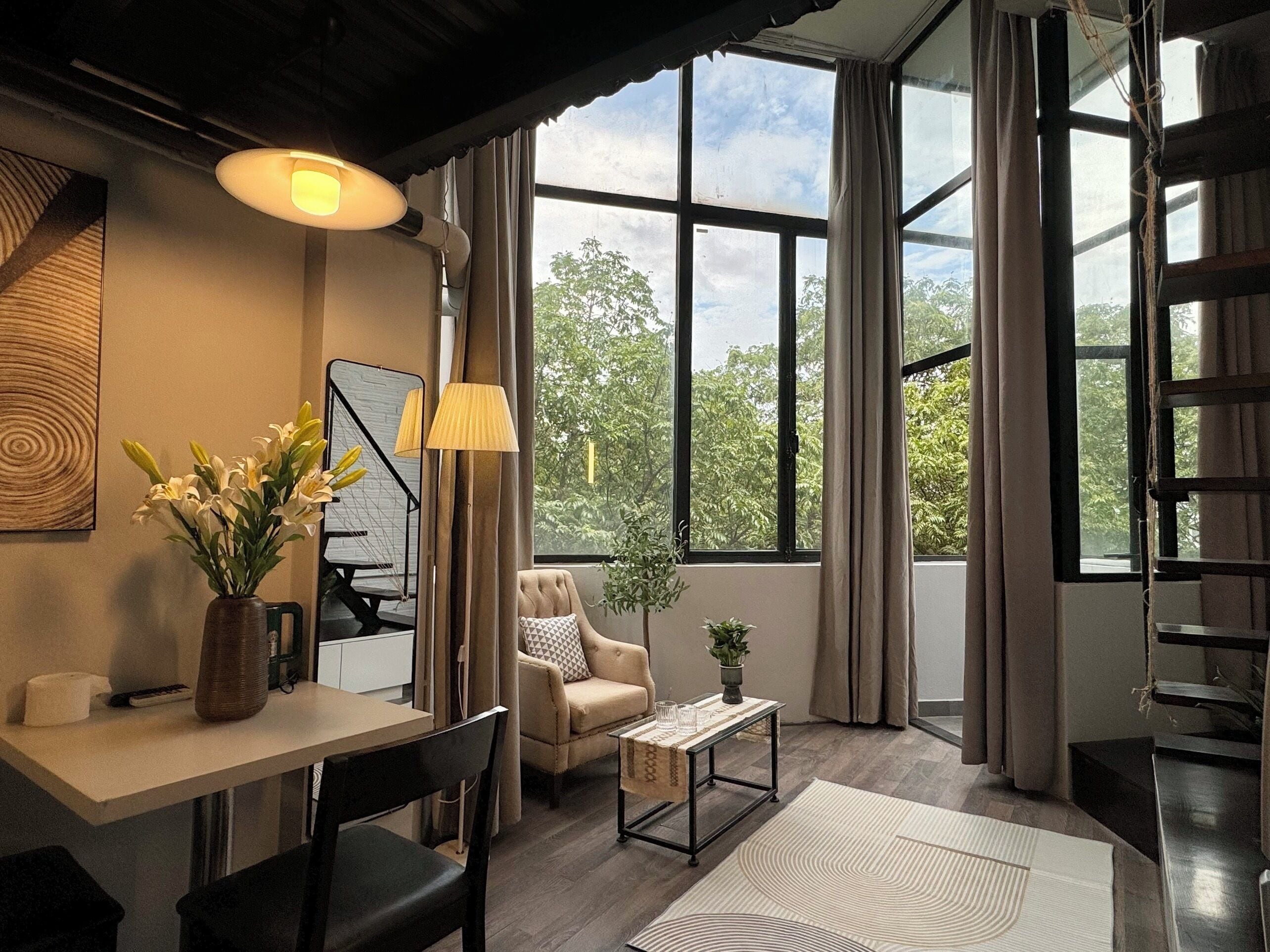 Una sala de estar moderna con un sofá, una mesa de centro y un comedor con mesa y sillas. Amplias ventanas ofrecen vistas al exterior.