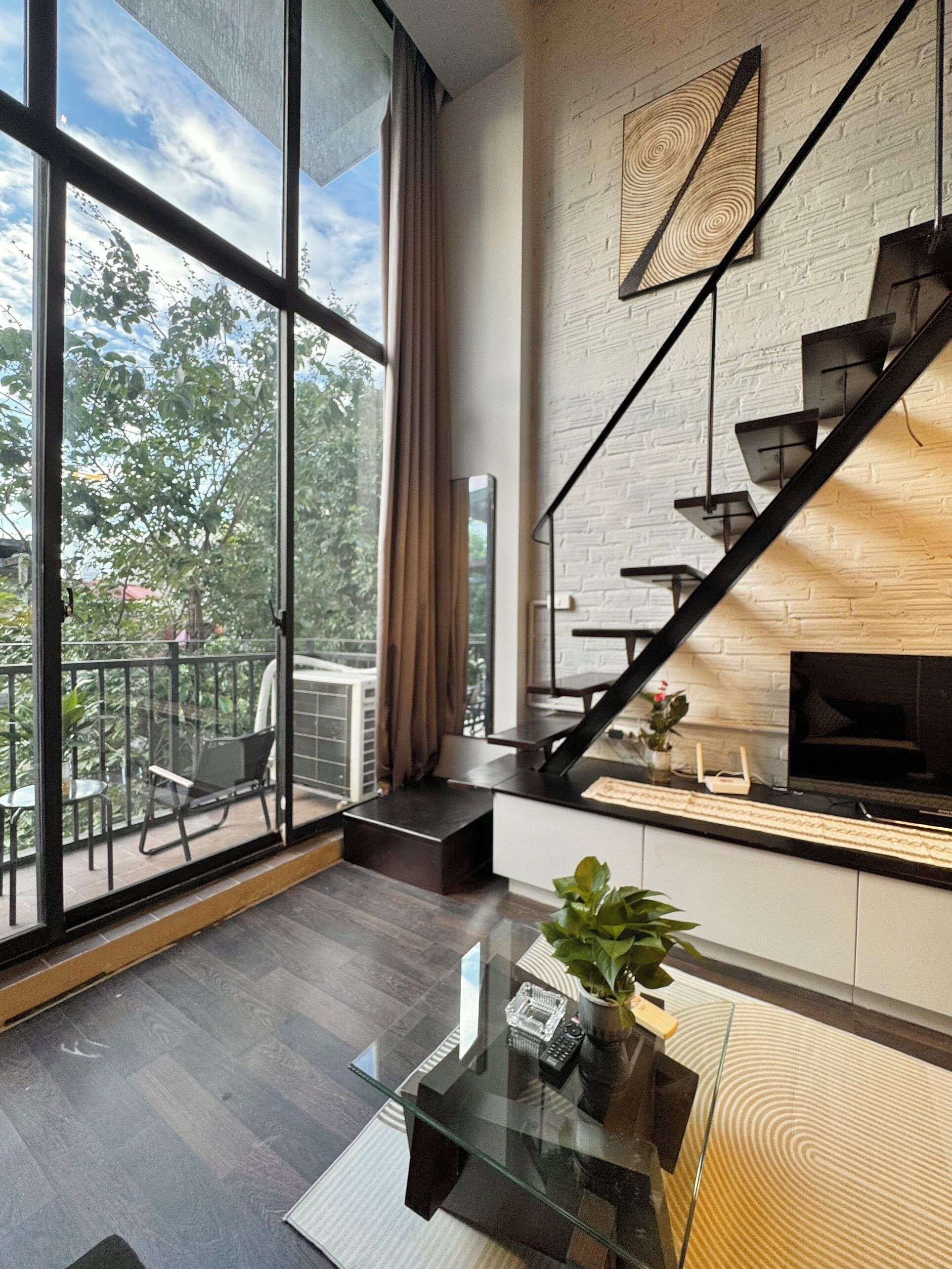 A modern living room with a large glass window, a fireplace, and a staircase.