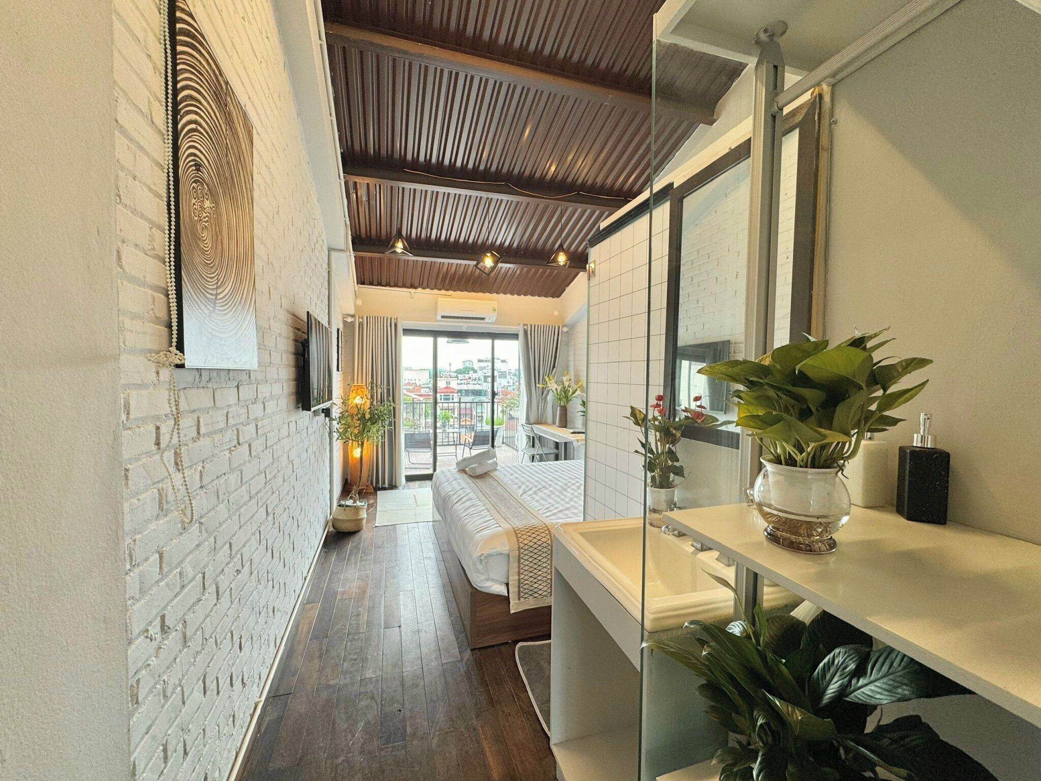 A modern hotel room with a brick wall, a wooden ceiling, a large window, and a balcony with a view.