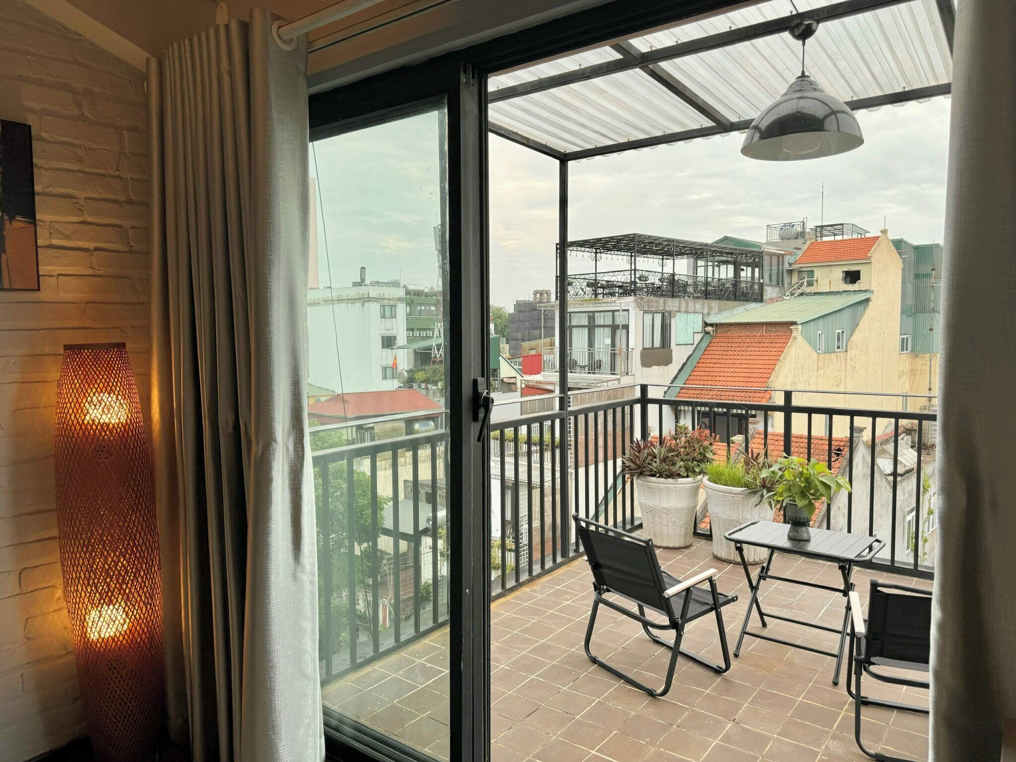 A balcony with a table and chairs, potted plants, and a view of surrounding buildings.