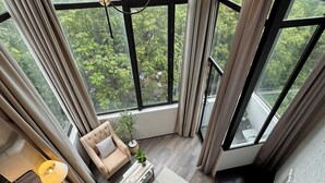 Un apartamento en un edificio alto con un gran ventanal que ofrece vistas a la ciudad, una zona de estar acogedora con un sofá y una mesita, y una escalera que sube a un piso superior.