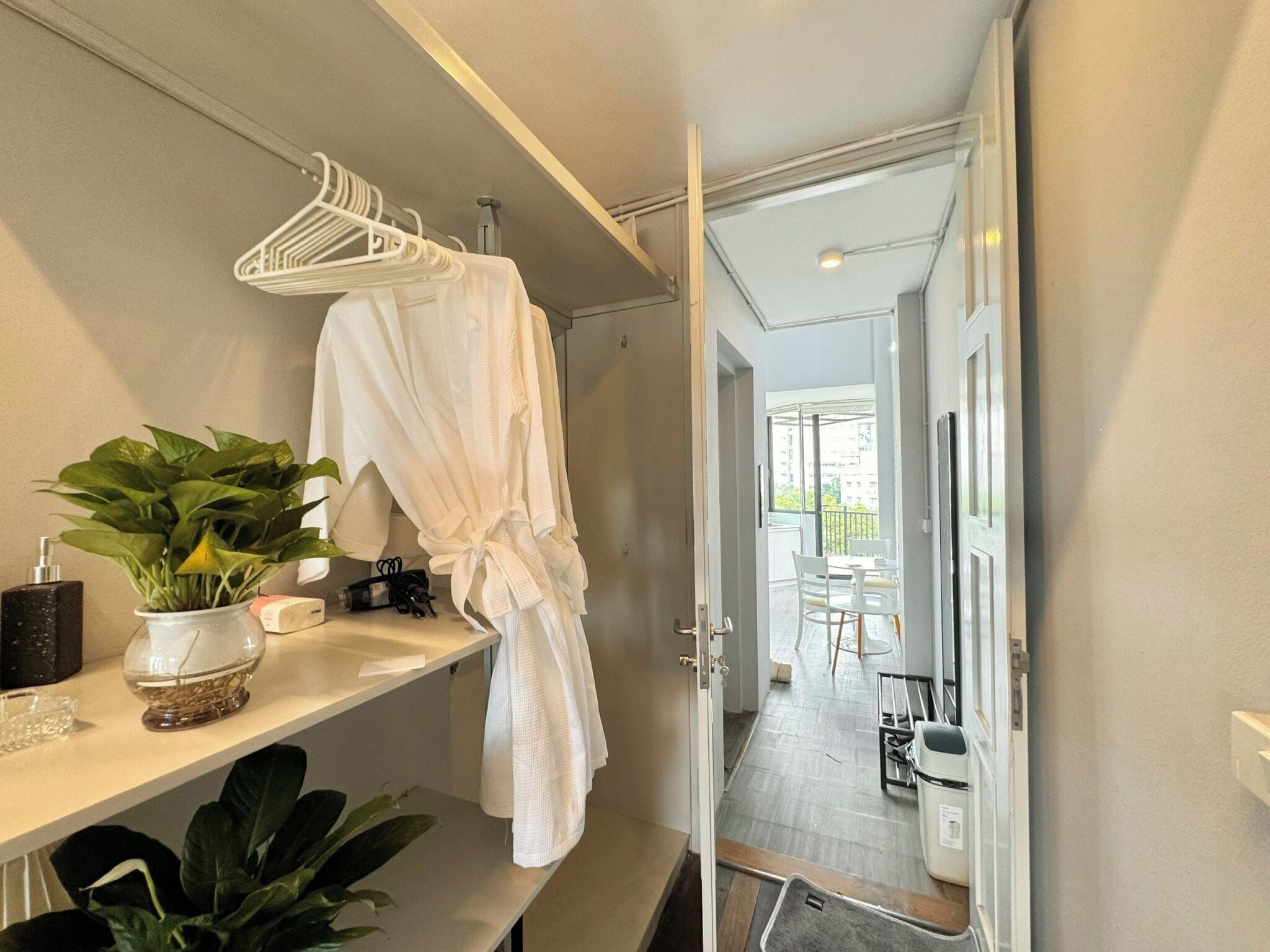 A bathroom with a towel rack, a potted plant, and a white robe hanging on the wall.