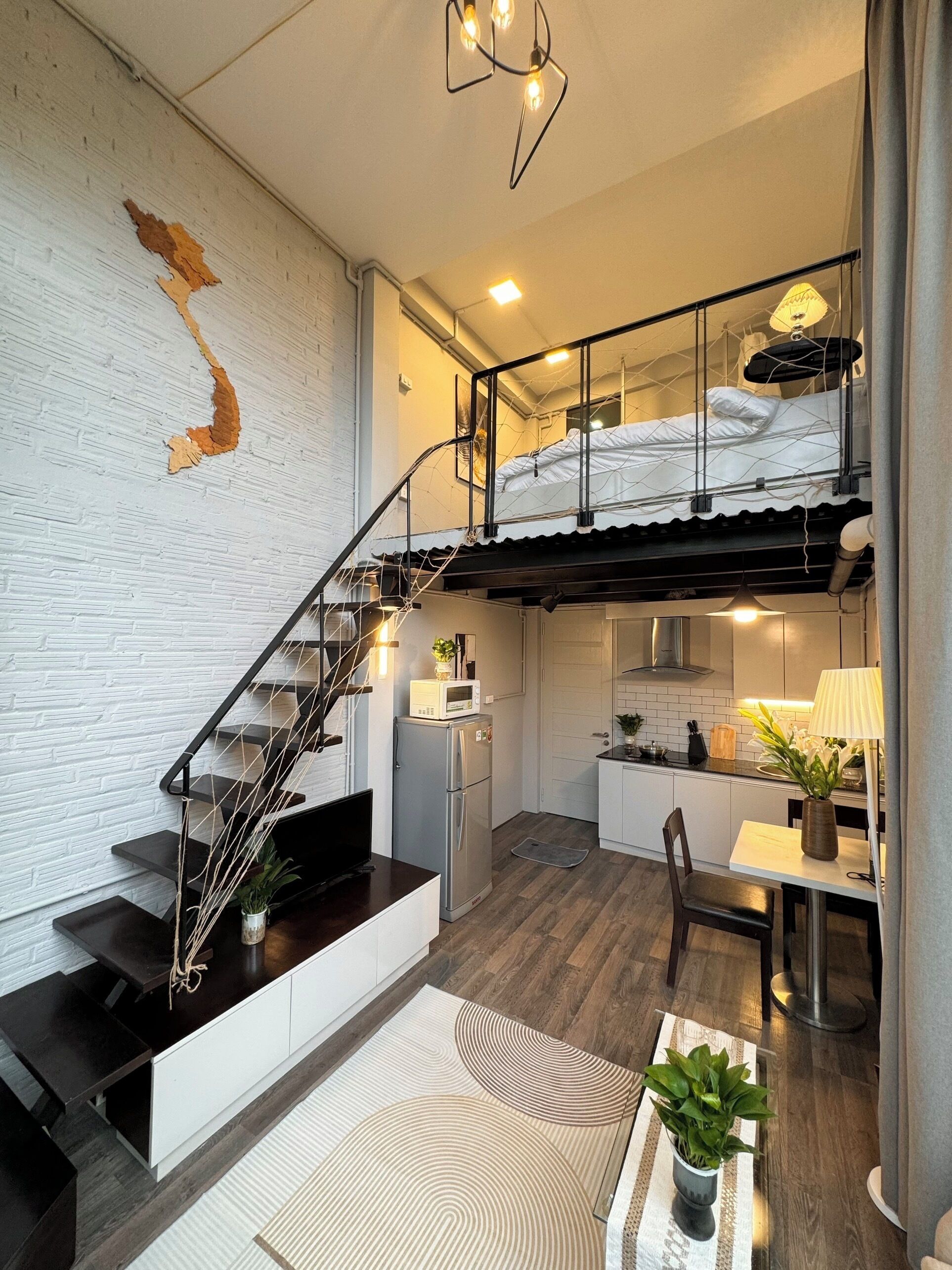 A modern loft apartment with a staircase leading to a loft bed, a kitchen with white cabinets, and a dining area with a table and chairs.