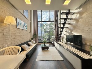 A modern living room with a sofa, a coffee table, a TV, and a staircase. - The Little Hanoi (Hanoi)