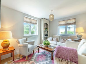 A living room with a sofa, armchairs, a coffee table, a bookshelf, and a window with curtains.