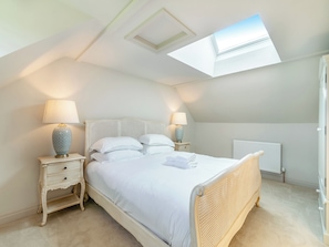 Une chambre avec un puits de lumière, un lit avec une literie blanche, deux tables de chevet avec des lampes et un radiateur.