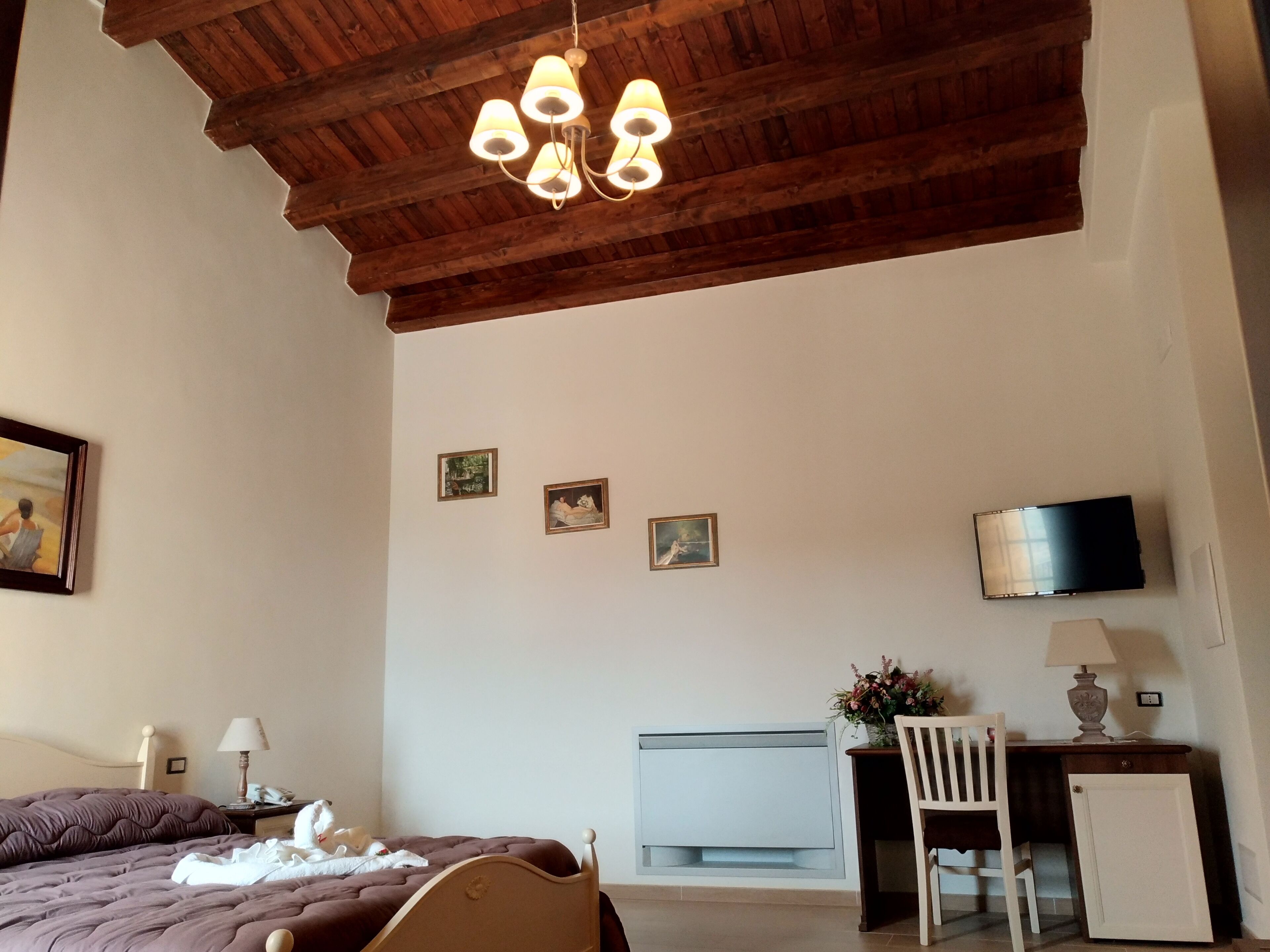 Une chambre avec un plafond en bois, un lit doté d’une tête de lit marron, un bureau avec une chaise, une télévision et un petit meuble.