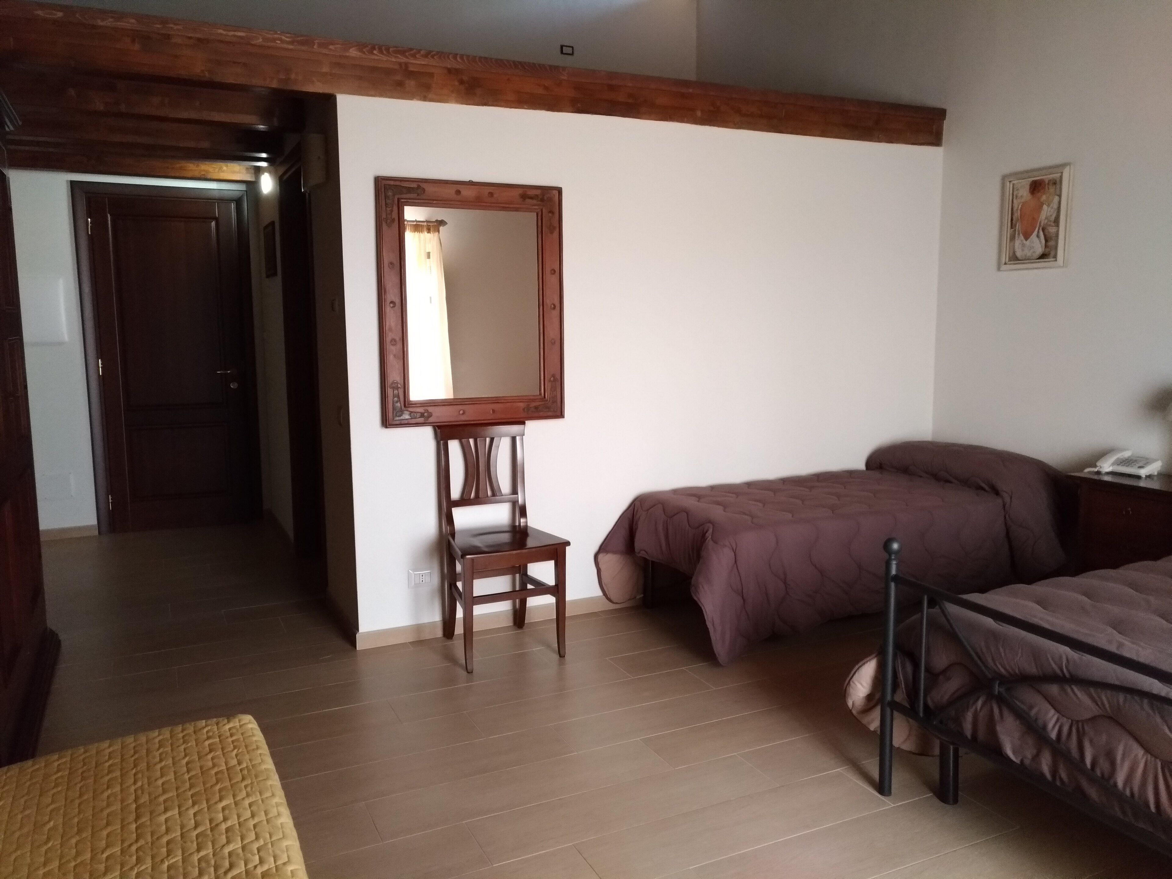 A bedroom with a wooden headboard, a bed with a brown duvet, a bedside table with a lamp, and a wooden chair.