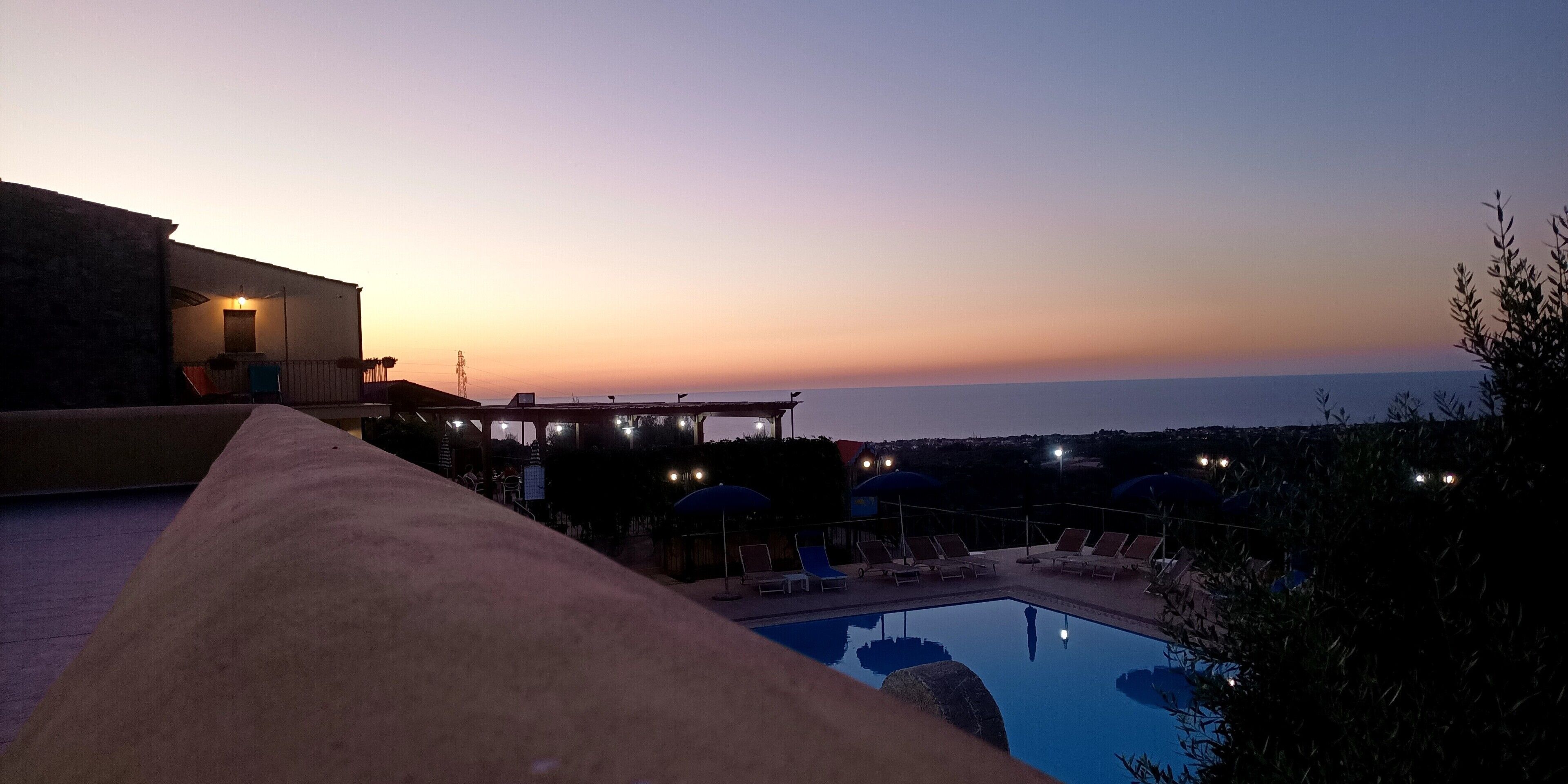 Area piscina con lettini e ombrelloni, vista sull'acqua al tramonto.