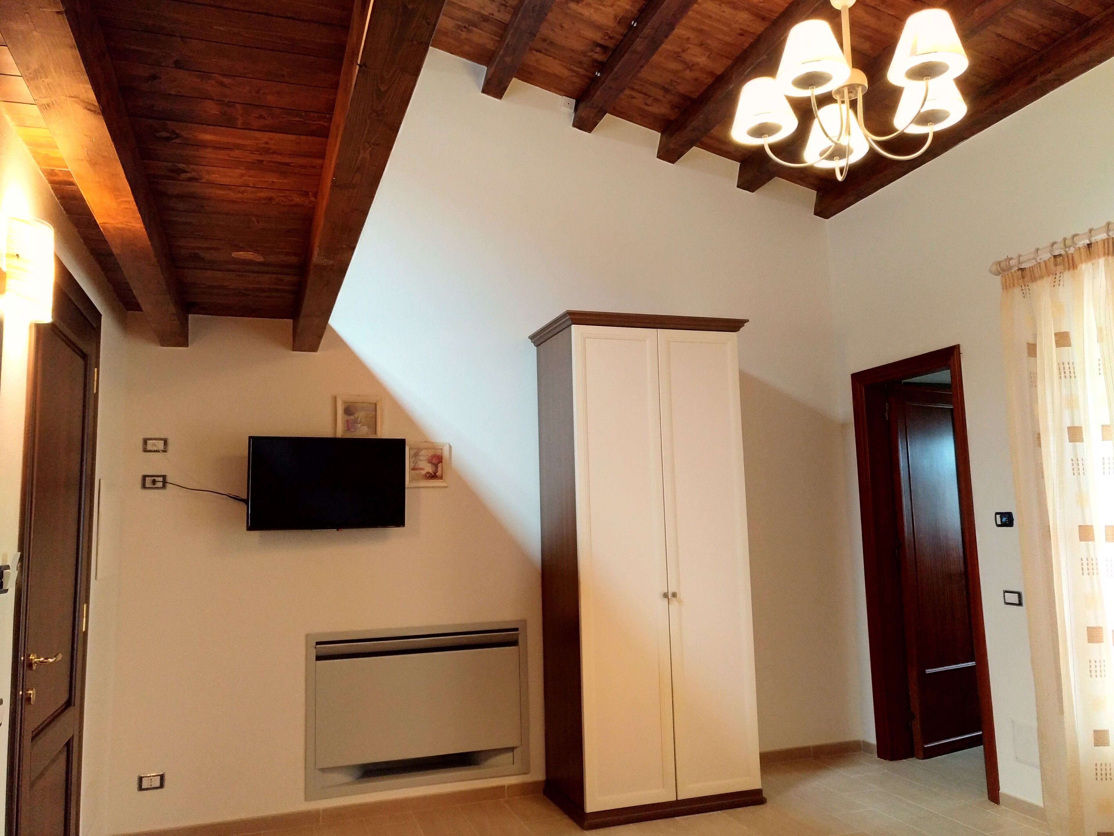 Una habitación con techo de madera, un armario blanco, un televisor montado y una puerta.