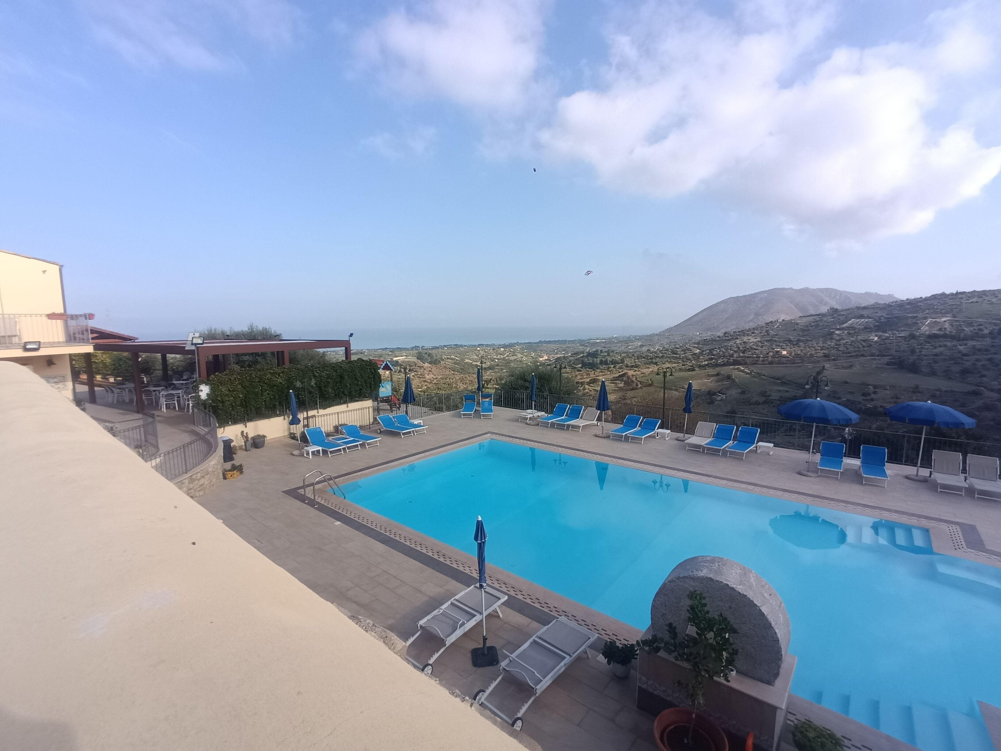 A pool area with lounge chairs and umbrellas, a view of the landscape, and a clear sky.